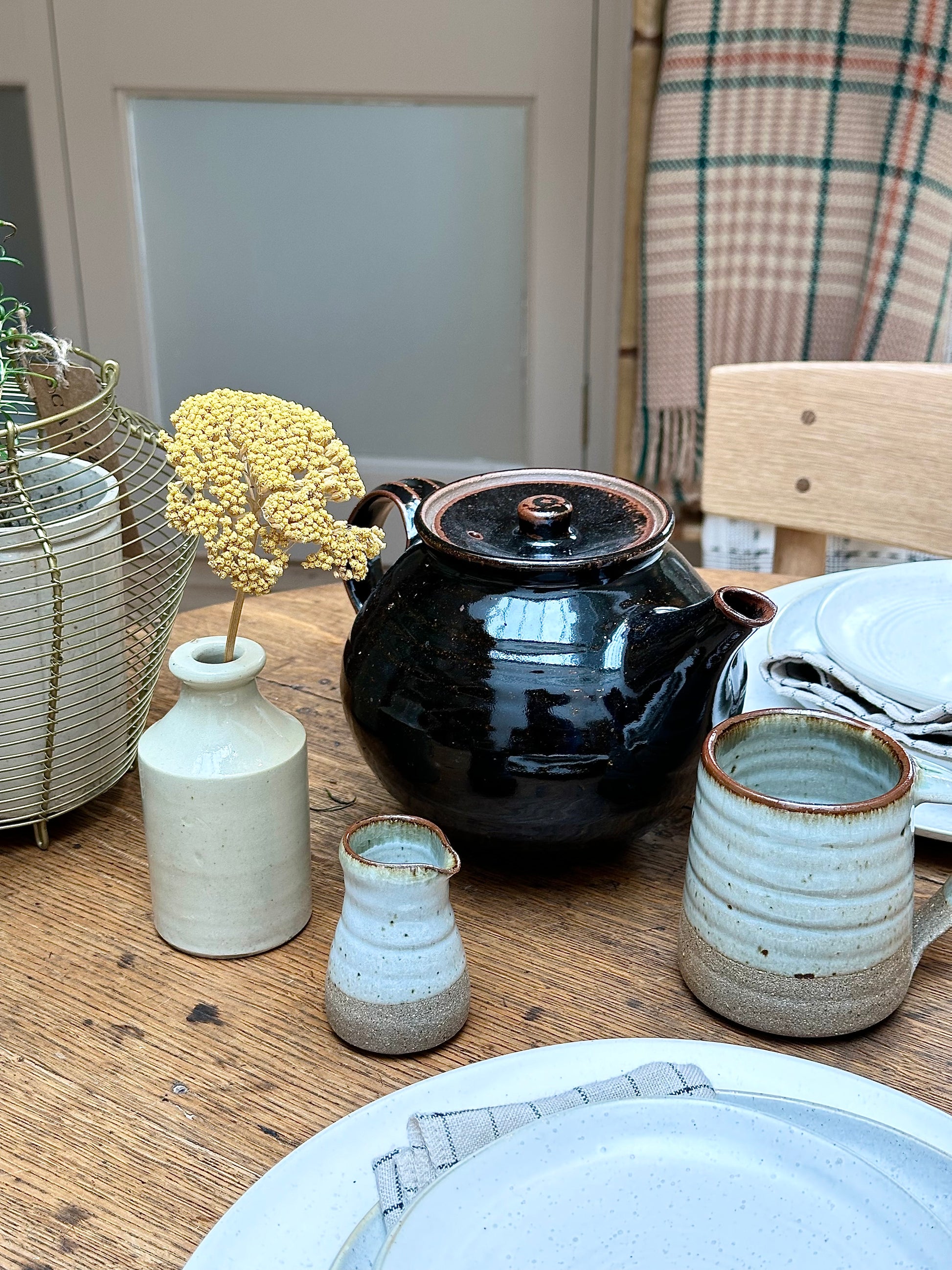 A Leach Pottery stoneware pourer with a 100ml capacity, displayed alongside a Leach teapot and mug on a wooden surface.