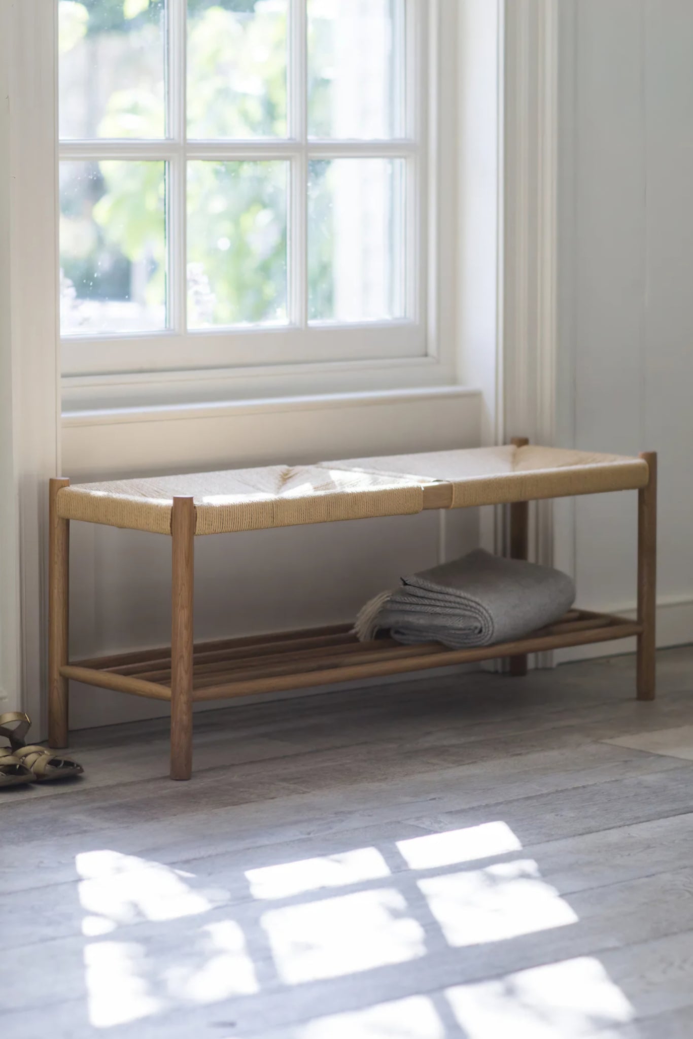 Wooden bench with woven top in a bright room with large windows.