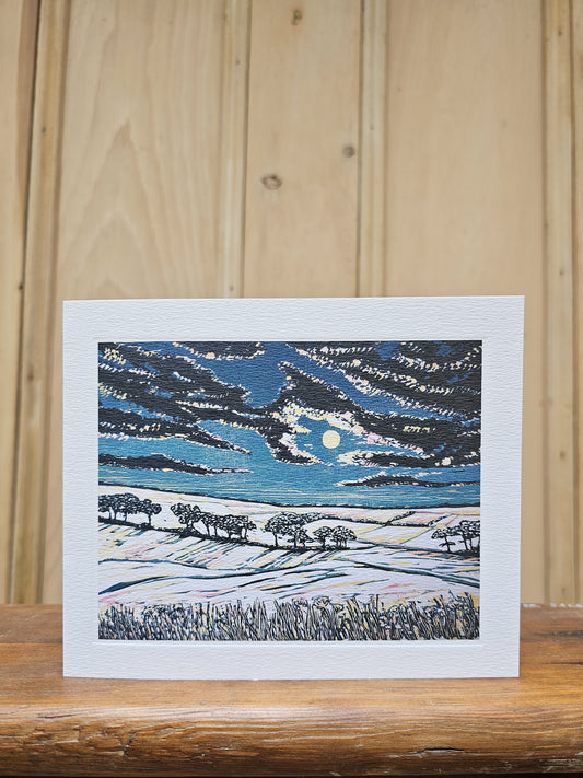 Greeting card reproducing Louise Stebbing's linocut print Full Moon, showing a pale moon breaking through dramatic dark clouds over a snowy hillside with silhouetted trees
