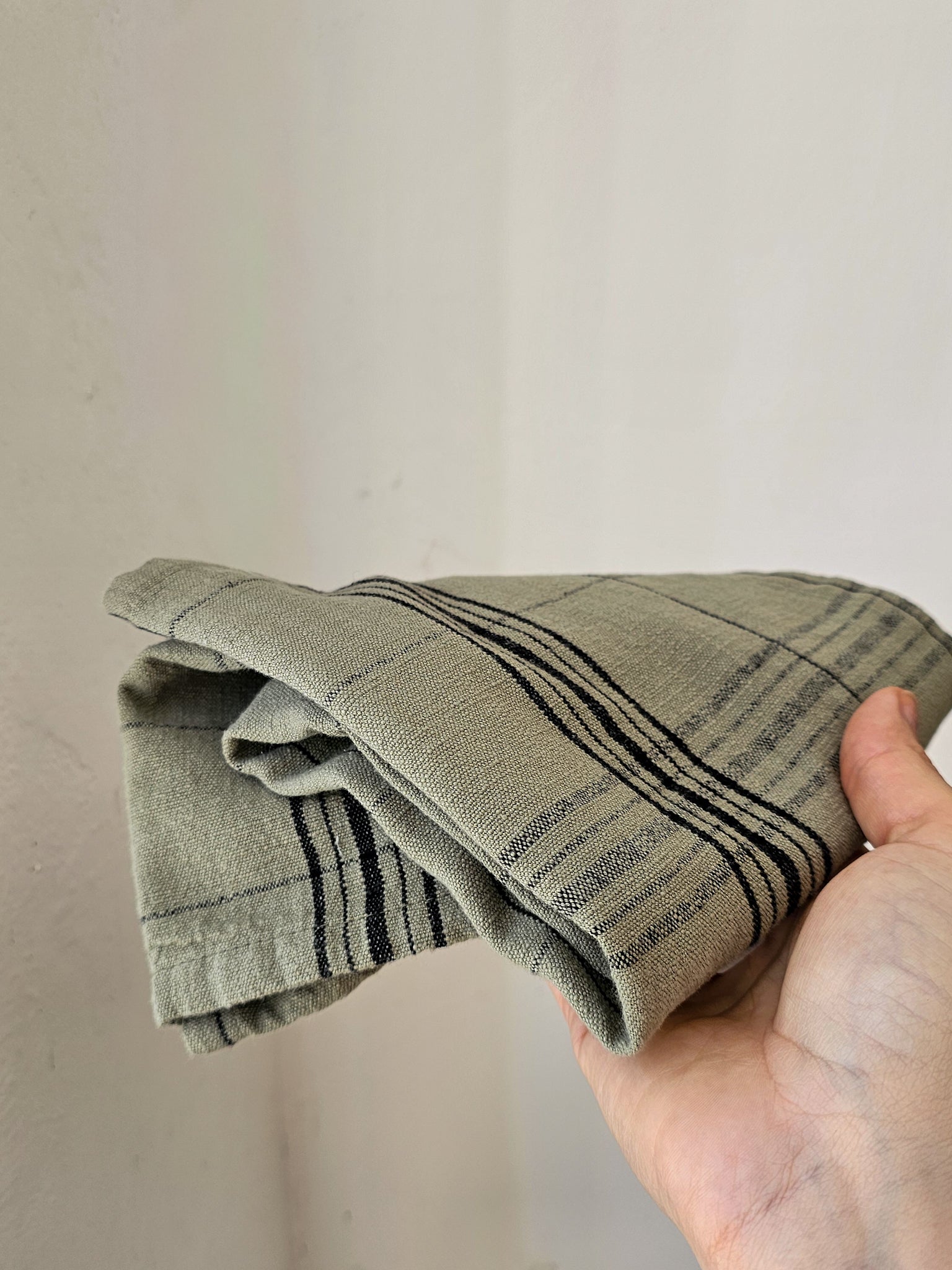 A folded cotton kitchen towel with black stripes, held in a person's hand against a plain off-white wall.