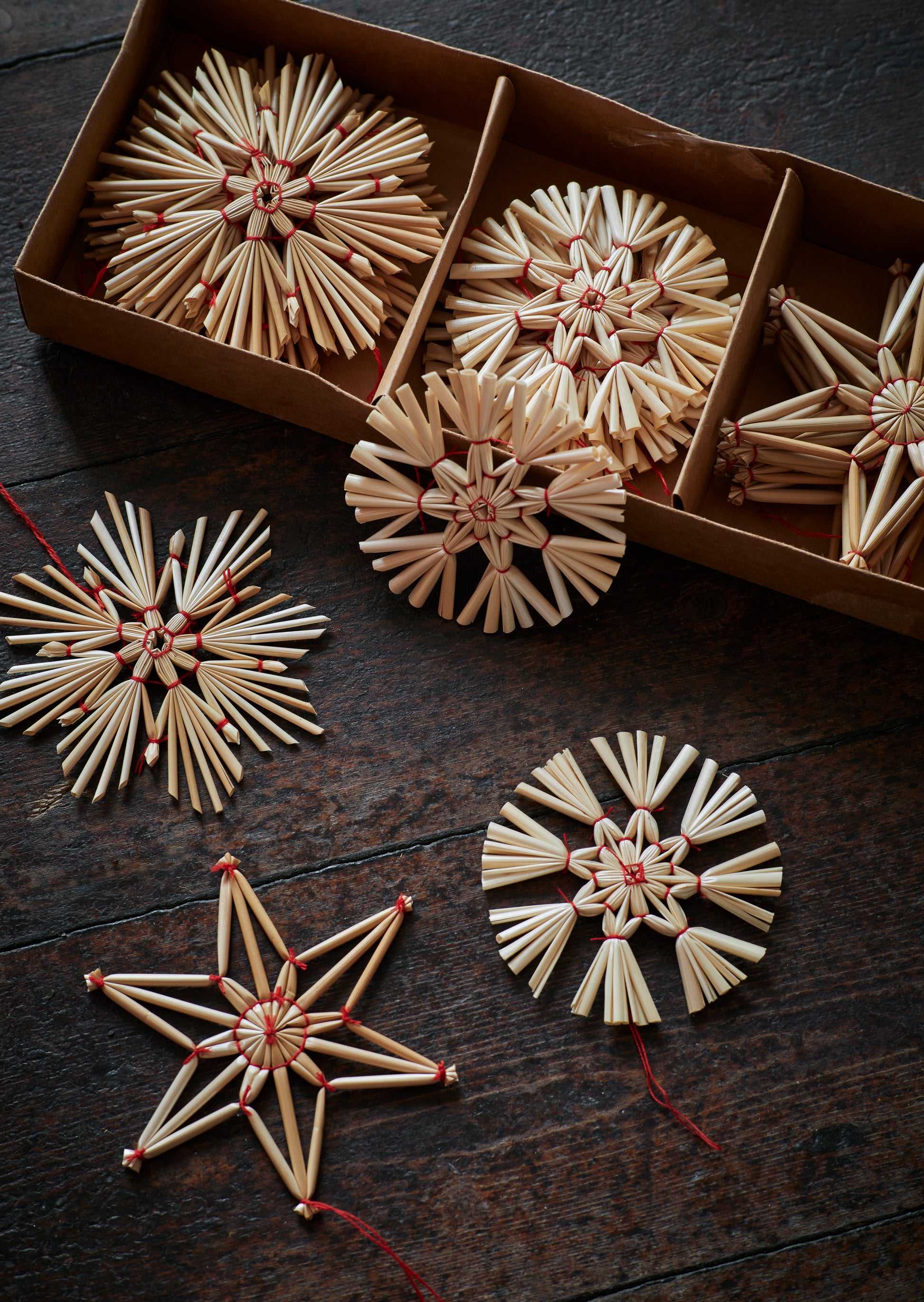 Madam Stoltz straw star ornaments displayed in box and scattered on dark wood table