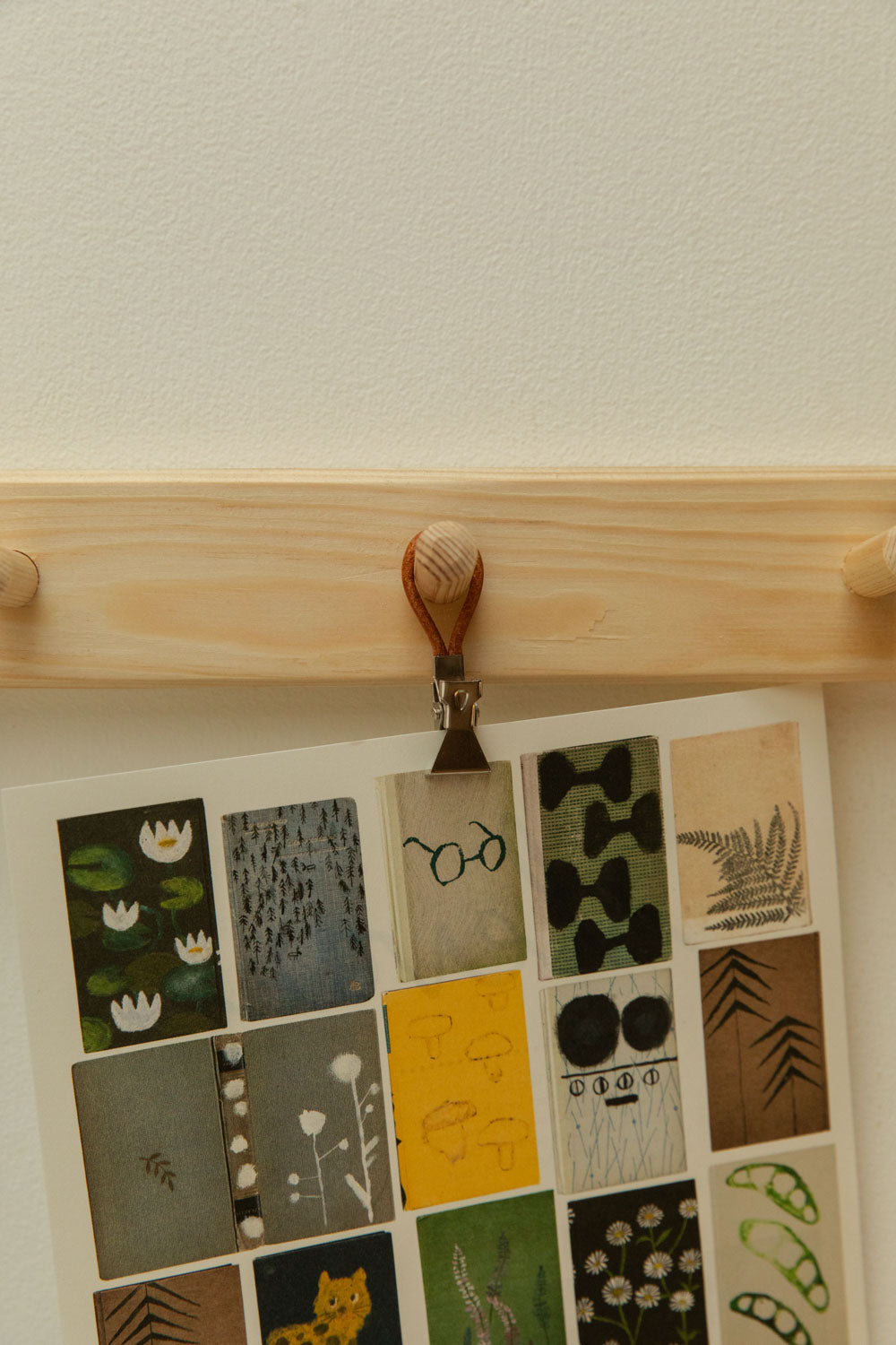 Close-up of Meraki towel clip in silver and leather hanging a botanical collage print card from a pine shaker peg rail.