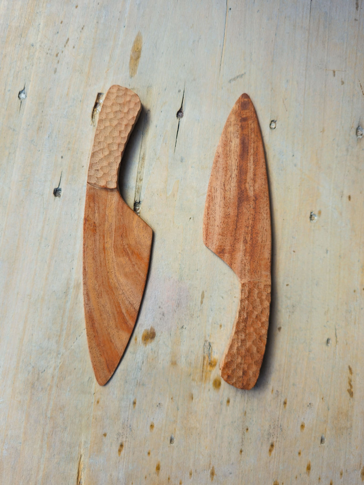 Two small wooden knife-shaped tools with textured handles, displayed side by side on a light wood background.