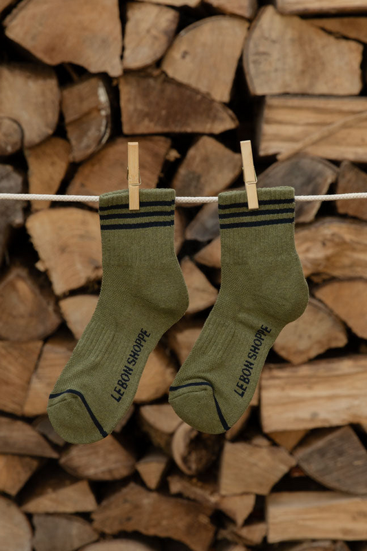 Le Bon Shoppe Girlfriend Socks in Sage with black stripes hanging on a line against stacked logs