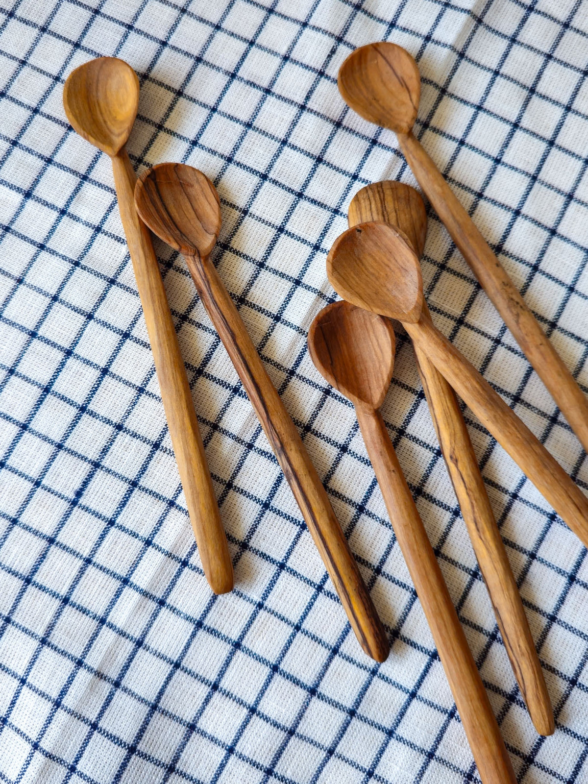 Six wooden spoons with visible wood grain patterns, arranged on a blue and white checkered cloth.
