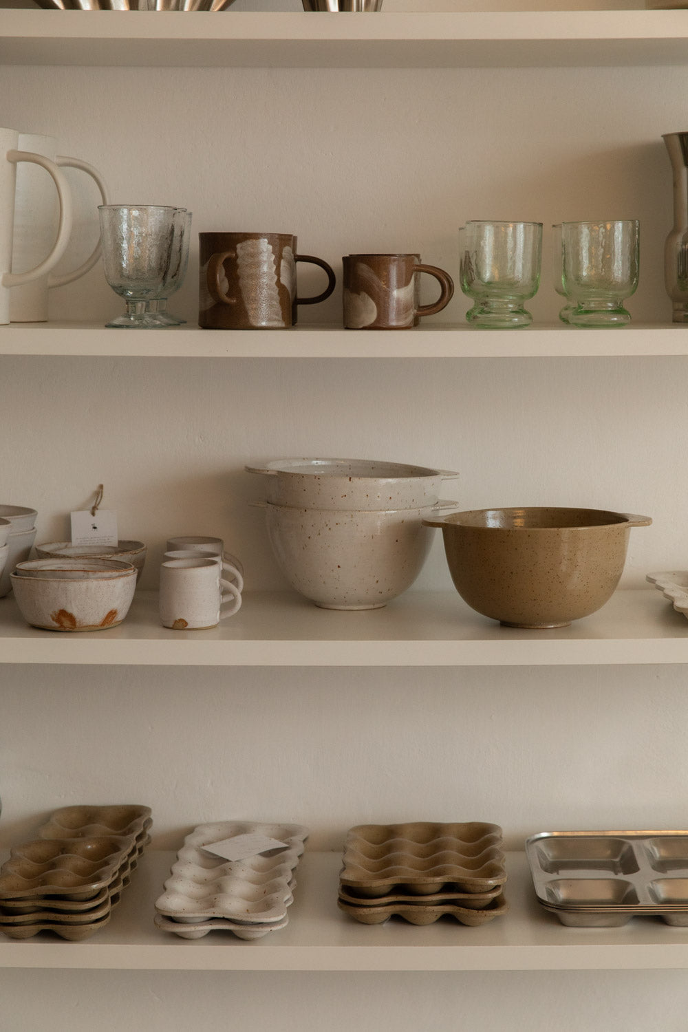 Open kitchen shelves stacked with handmade mugs, glass tumblers, speckled bowls and egg trays