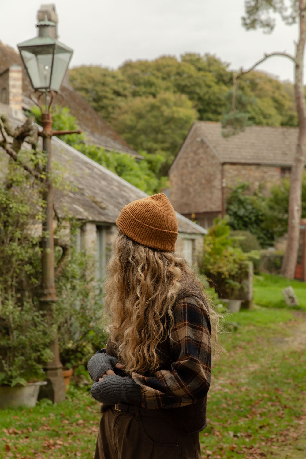 Woman in an orange ribbed beanie and check shirt on a Cornish village lane