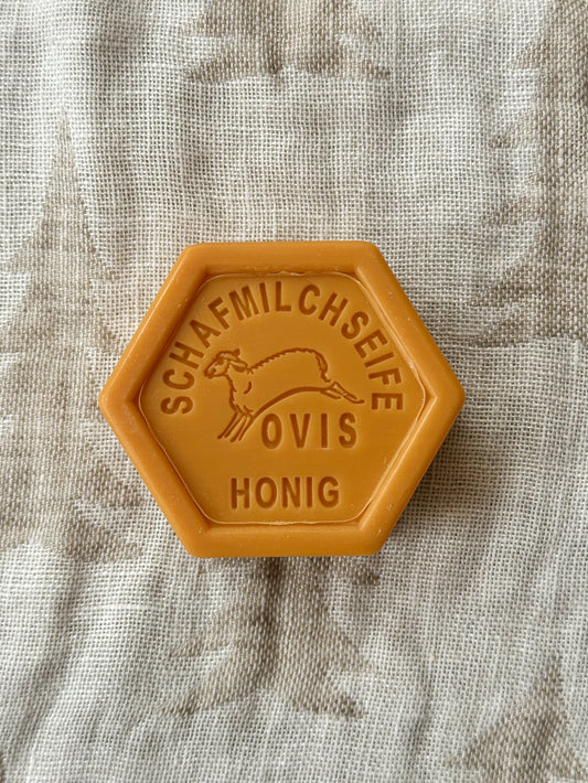 A hexagonal bar of soap with a solid yellow color and text on it, placed on a textured fabric surface.