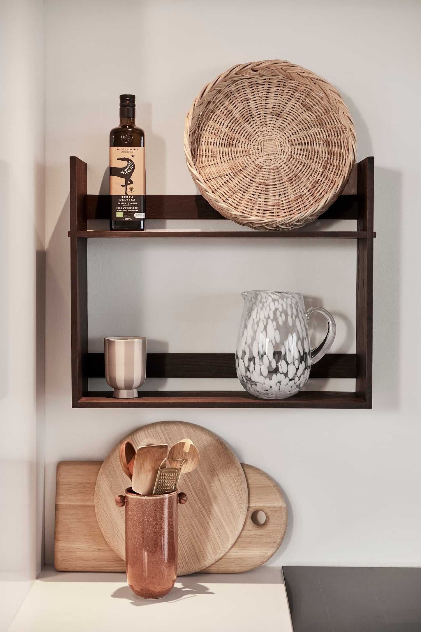 OYOY Maru Bread Basket in rattan on dark wood wall shelf styled with glass jug and striped ceramic cup