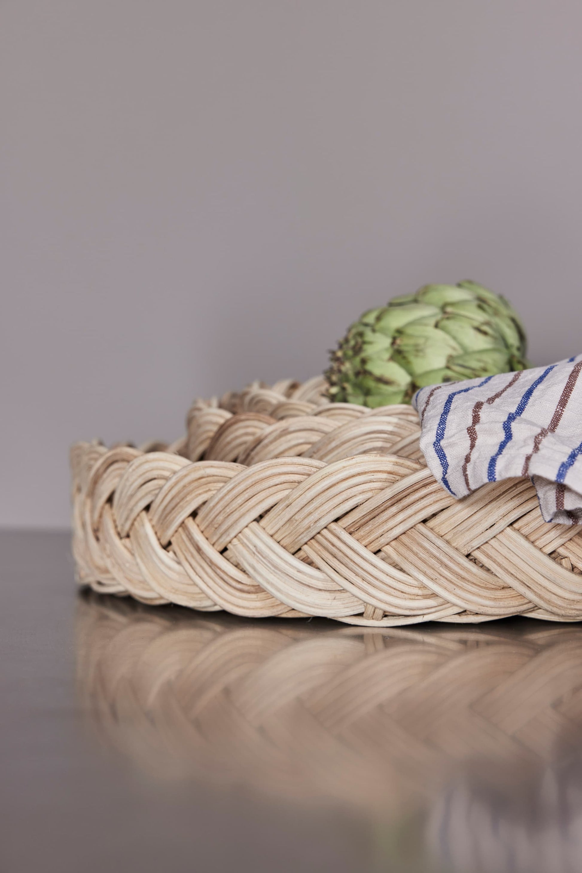 OYOY Maru Bread Basket in rattan close up with braided edge, artichoke and striped linen cloth
