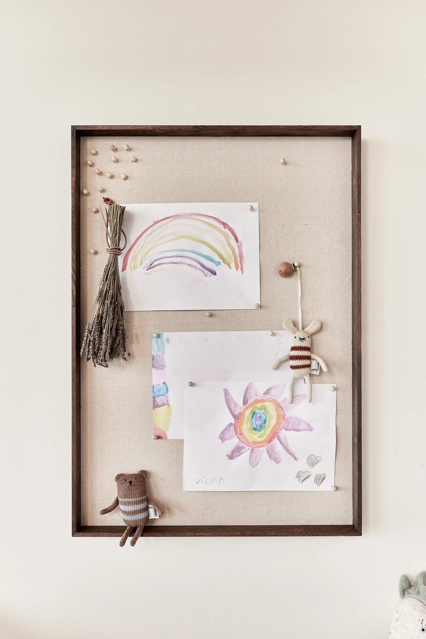 OYOY Peili Notice Board with dark wood frame styled with children's artwork, dried flowers and knitted toy figures