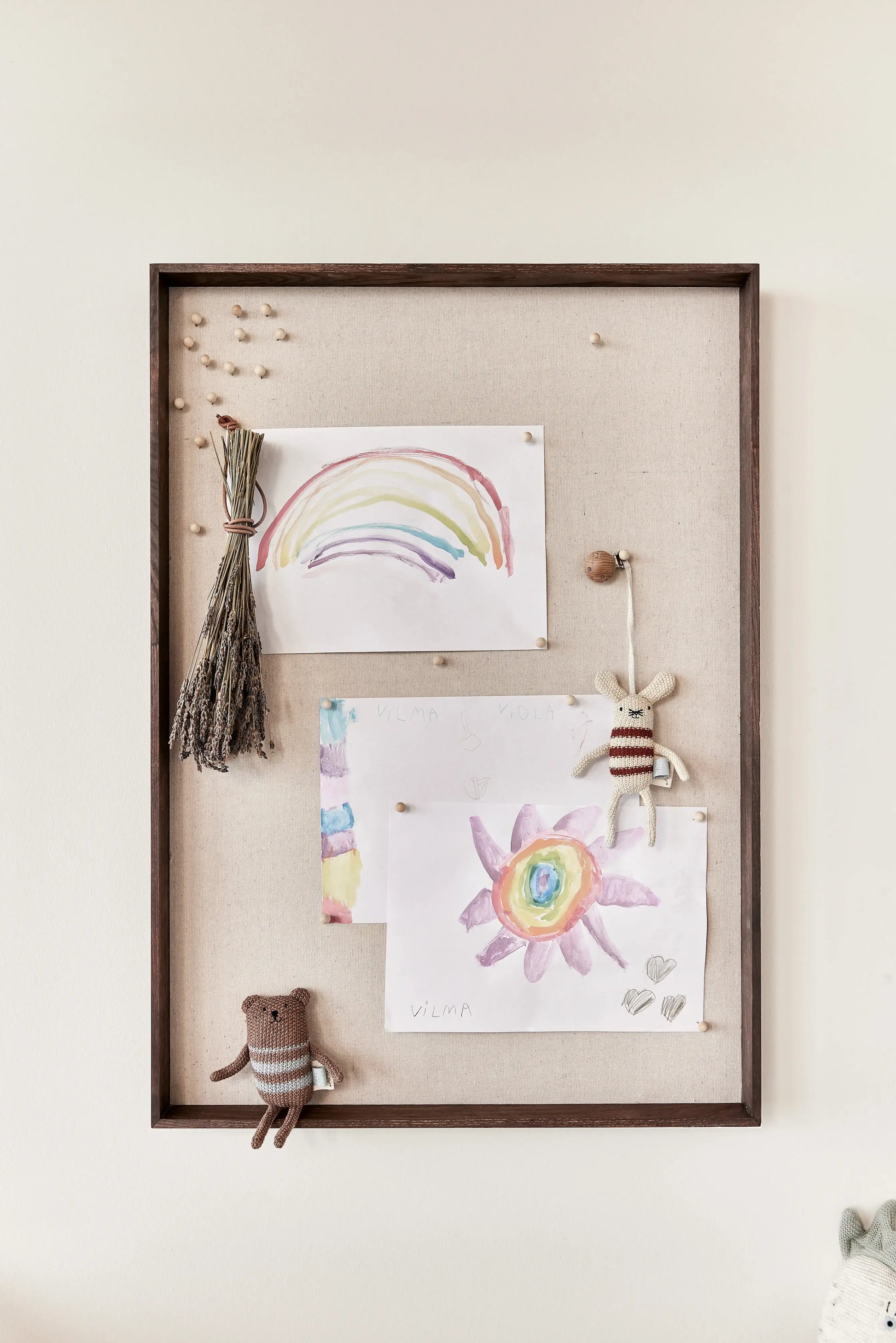 OYOY Peili Notice Board with dark wood frame styled with children's artwork, dried flowers and knitted toy figures