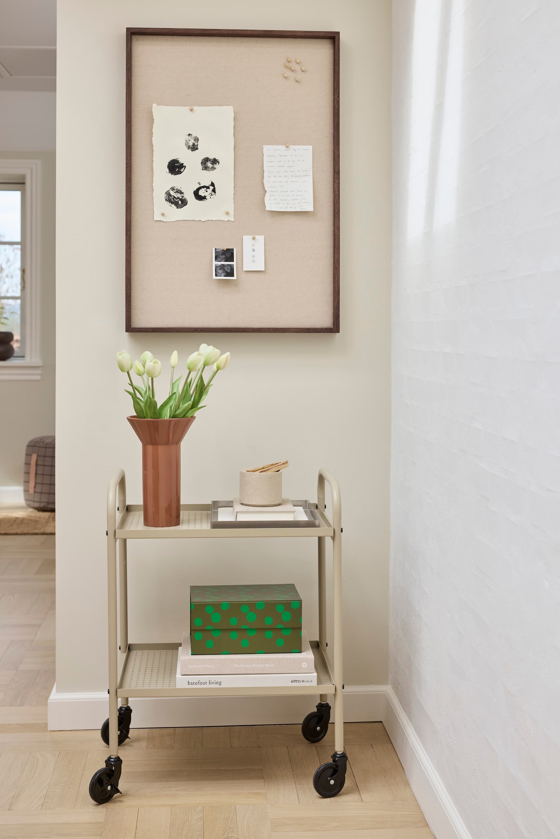 OYOY Peili Notice Board with dark wood frame styled with art prints and notes, above a trolley with tulips and books