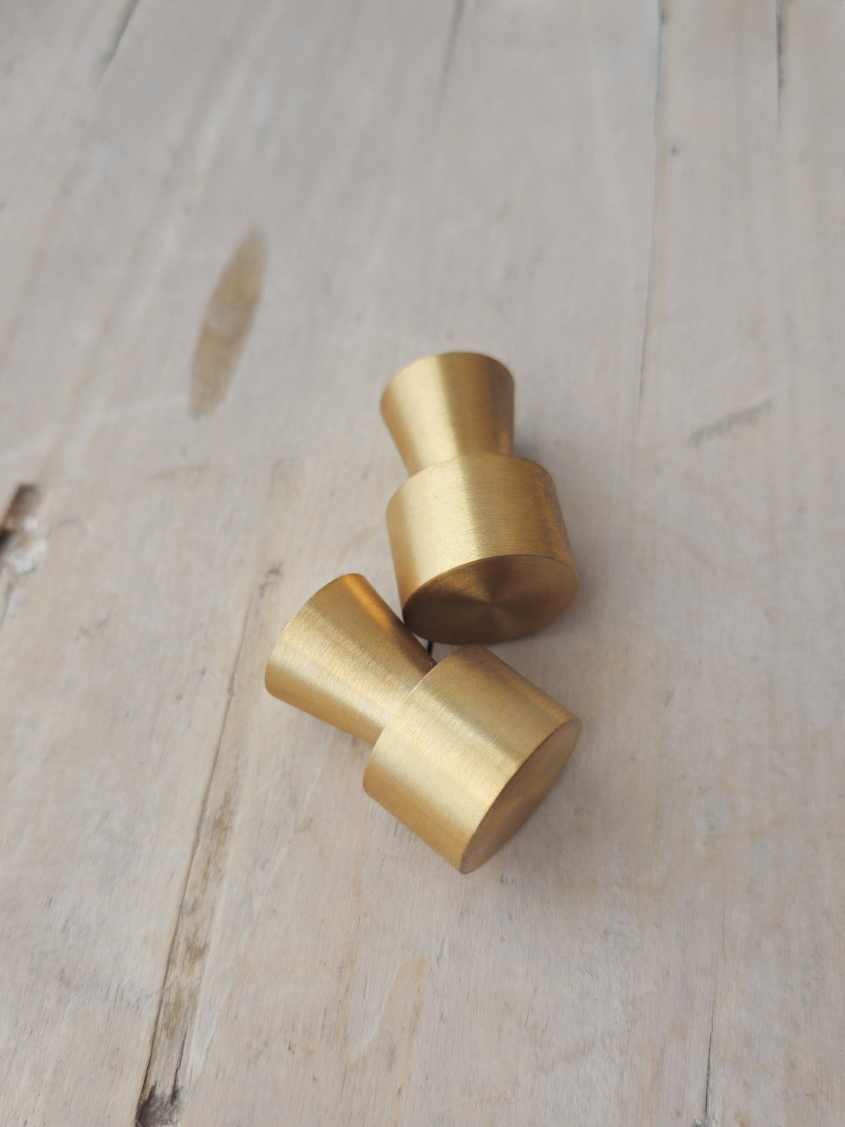 Two brass cabinet knobs with a brushed metallic finish, displayed on a light-colored wooden surface.