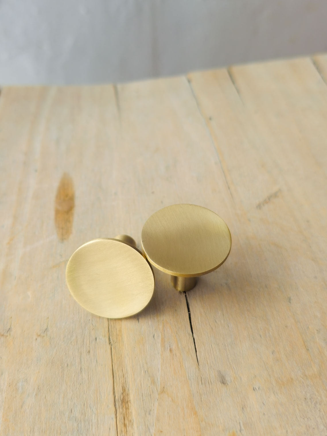 Two round brushed brass cabinet knobs resting on a light wood tabletop.