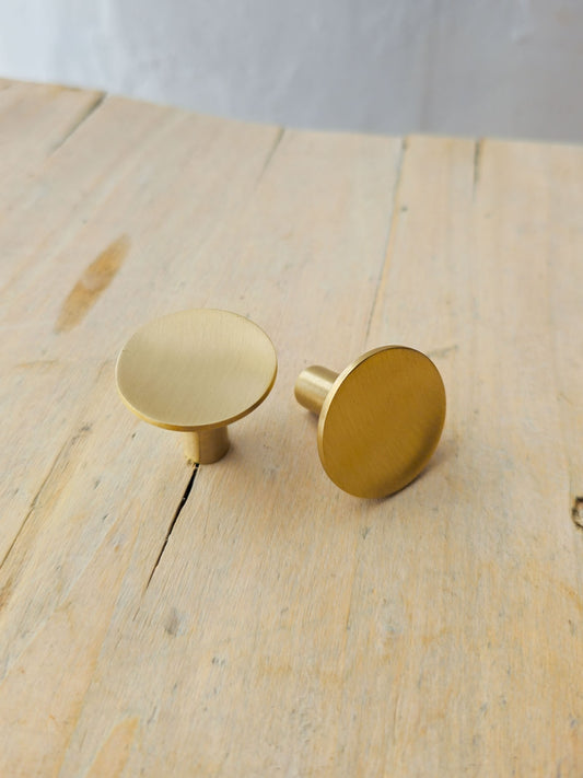 Two round brushed brass cabinet knobs resting on a light wood surface.