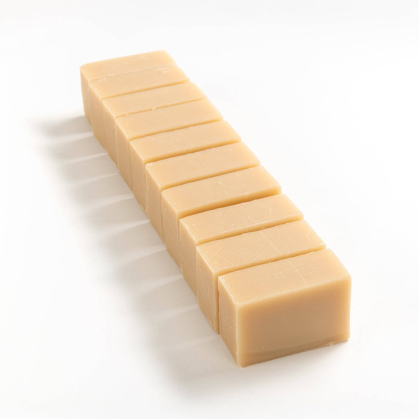 Row of patchouli and oat milk soap brick cut into smaller rectangular pieces on a white background