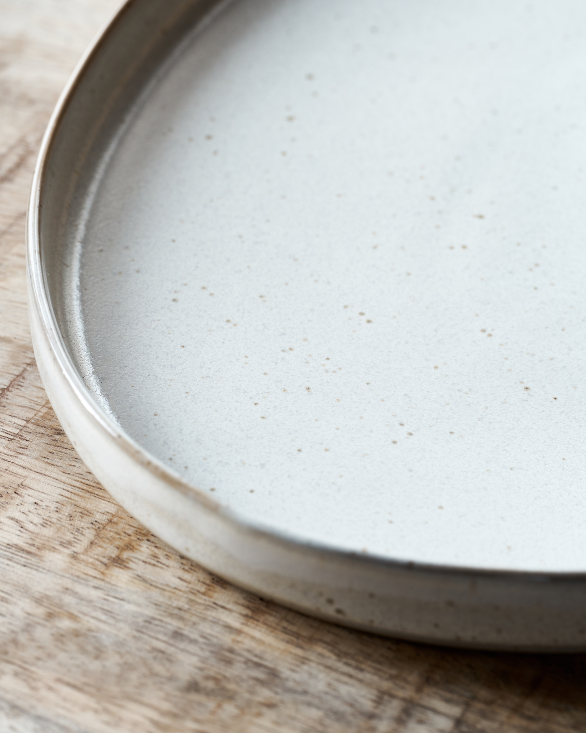Close up of a speckled white serving dish on a wooden table.