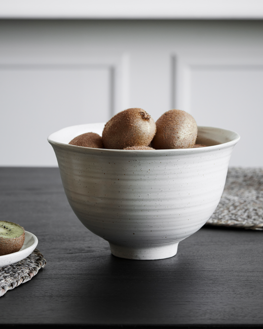 Large speckled white serving bowl holding kiwi's on a black table.