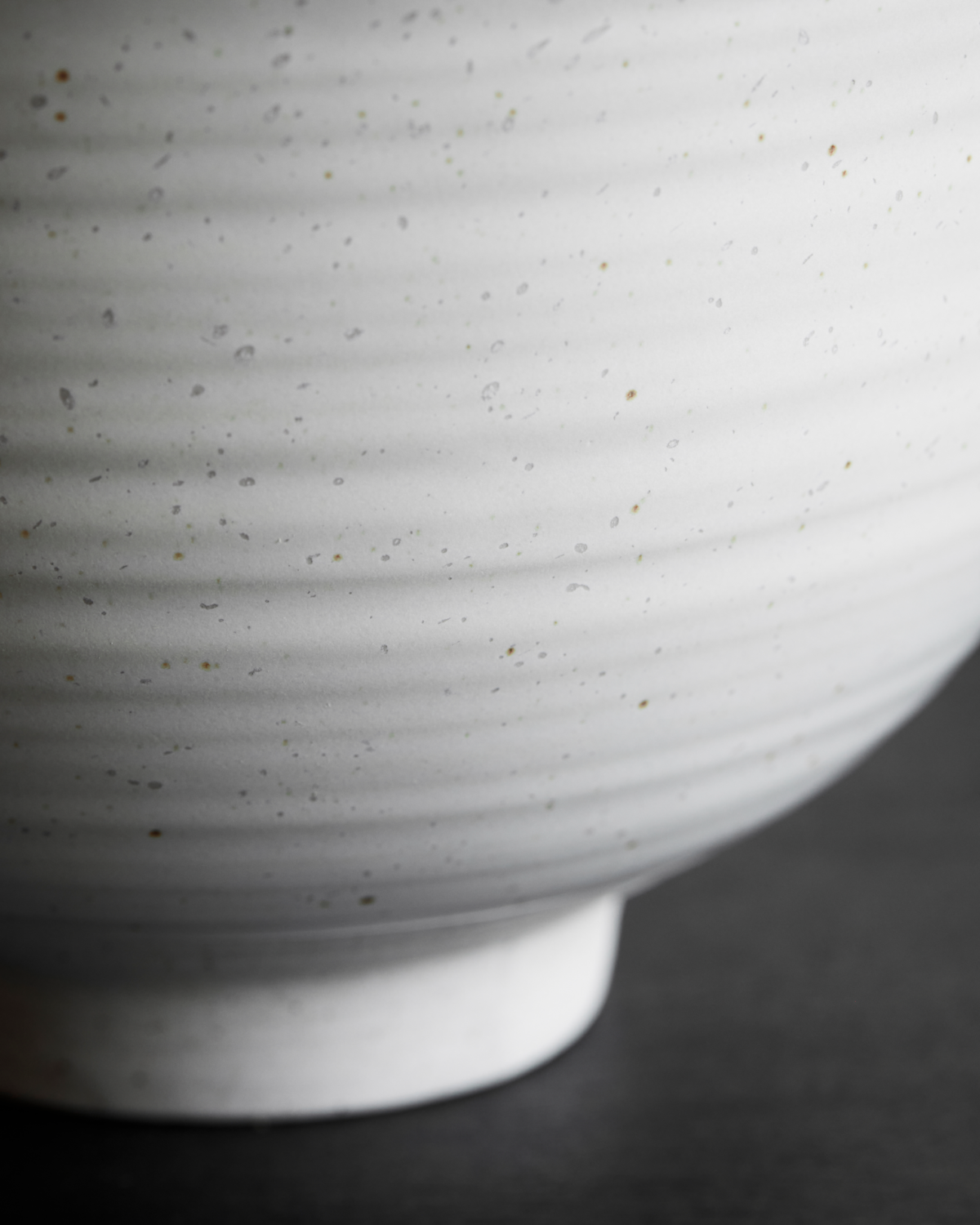 Close up of a speckled white stoneware serving bowl on a black background.