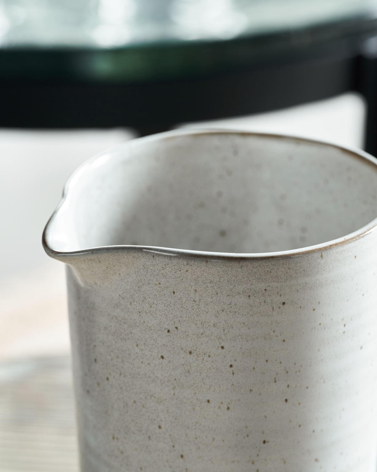 Close-up of a speckled white ceramic pitcher on a blurred background.
