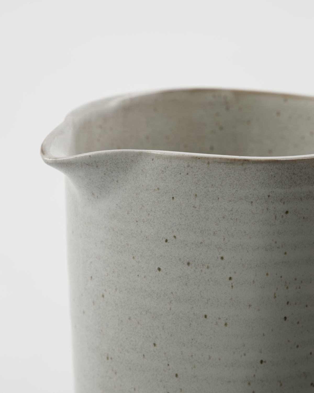 Close-up of a speckled white ceramic pitcher on a light background.