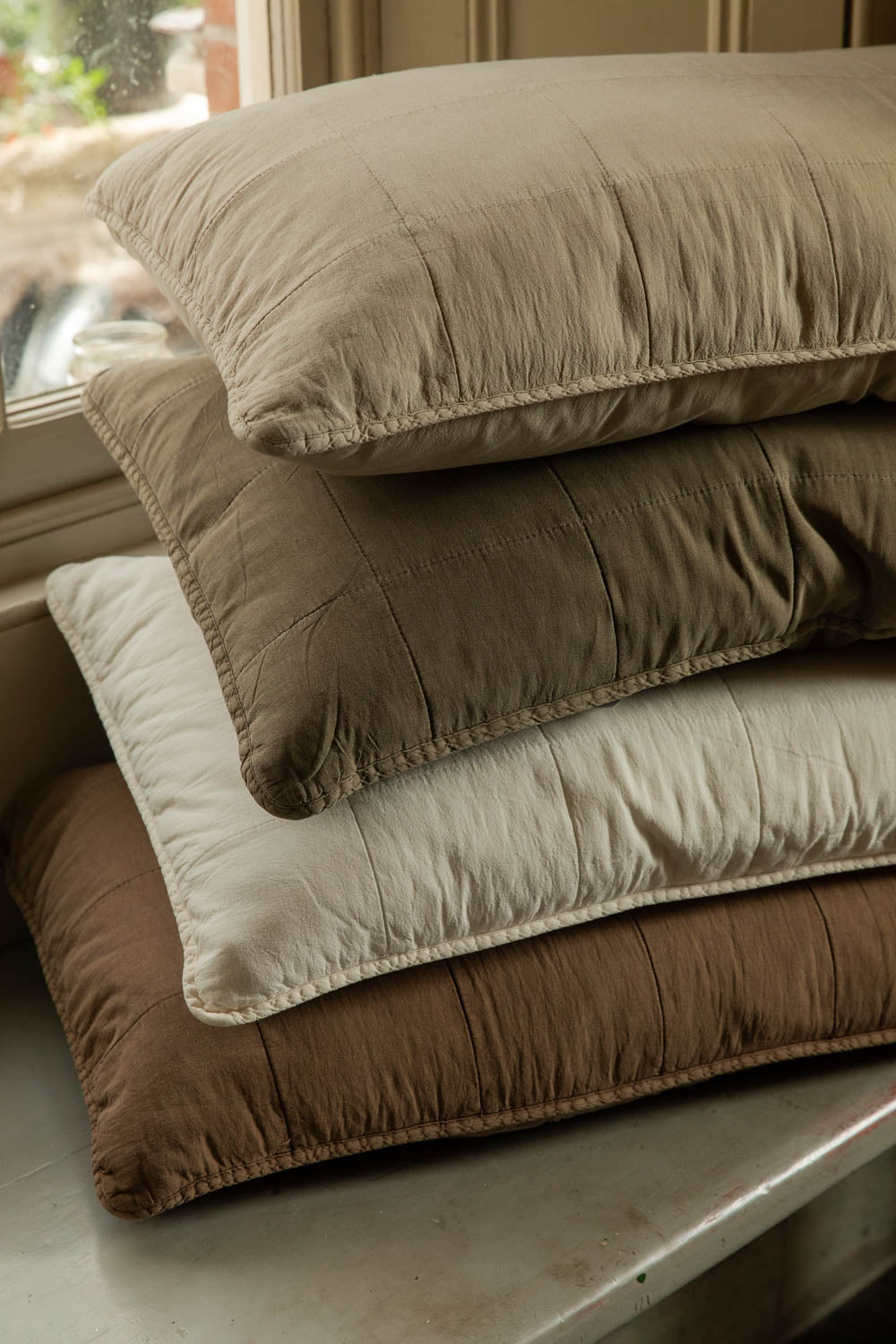 Close-up of stacked quilted cotton headboard cushions in soft neutral, green, white and brown tones