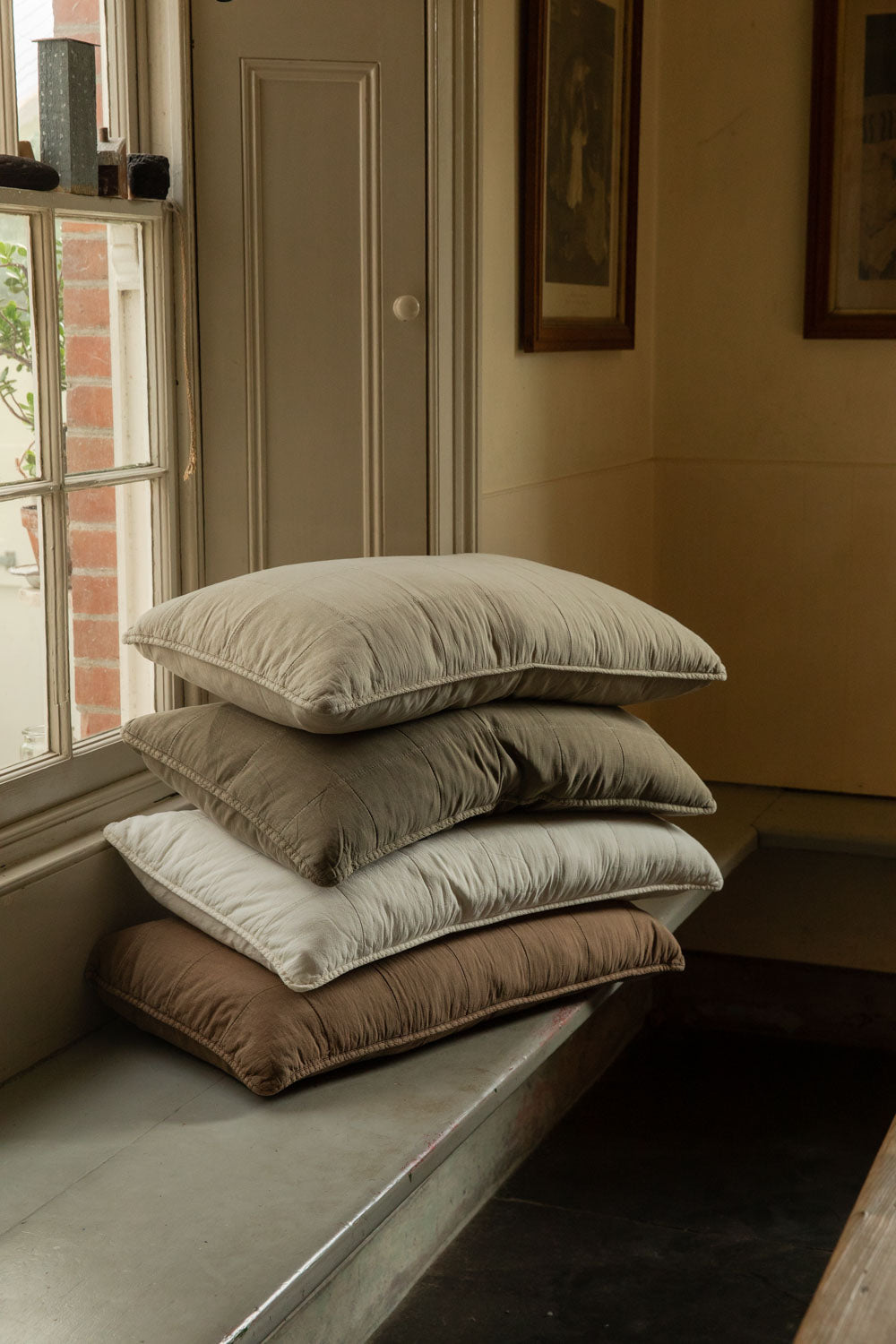 Stack of four quilted headboard cushions in butter cream, eucalyptus, fog and truffle on a window seat