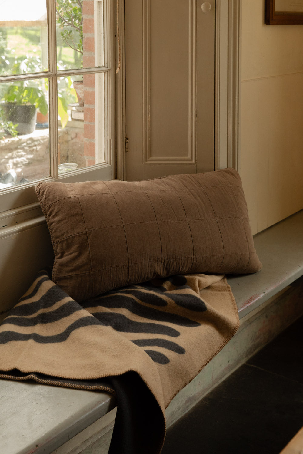 Truffle-brown quilted headboard cushion on a painted window seat, with a sand and black Pine lambswool blanket