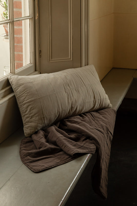 Fog quilted headboard cushion resting on a crumpled brown Soil stonewashed cotton quilt on a sunlit window seat