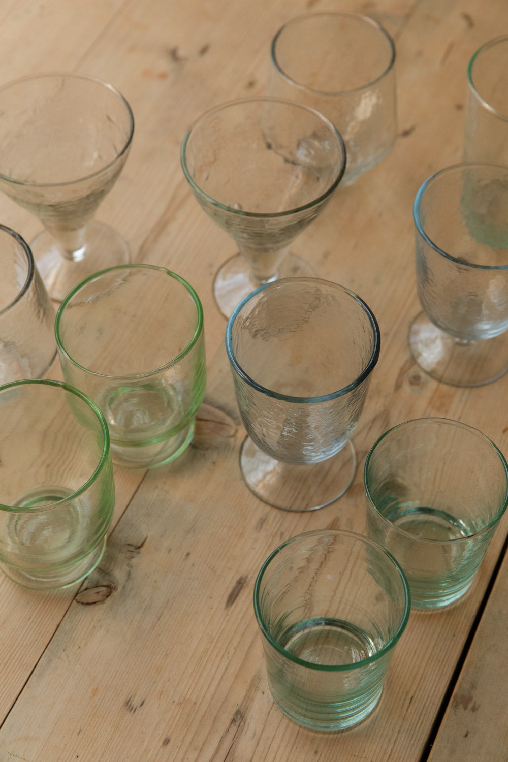 Overhead of green-tinted Meknes recycled glass tumblers with hammered and cut line glasses on a wooden table