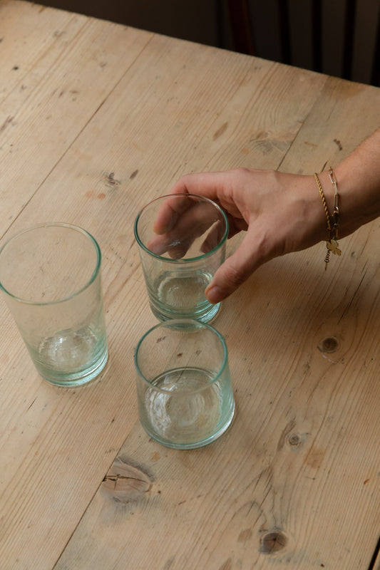 Hand reaching for a green-tinted hand-blown recycled glass tumbler on a pine table