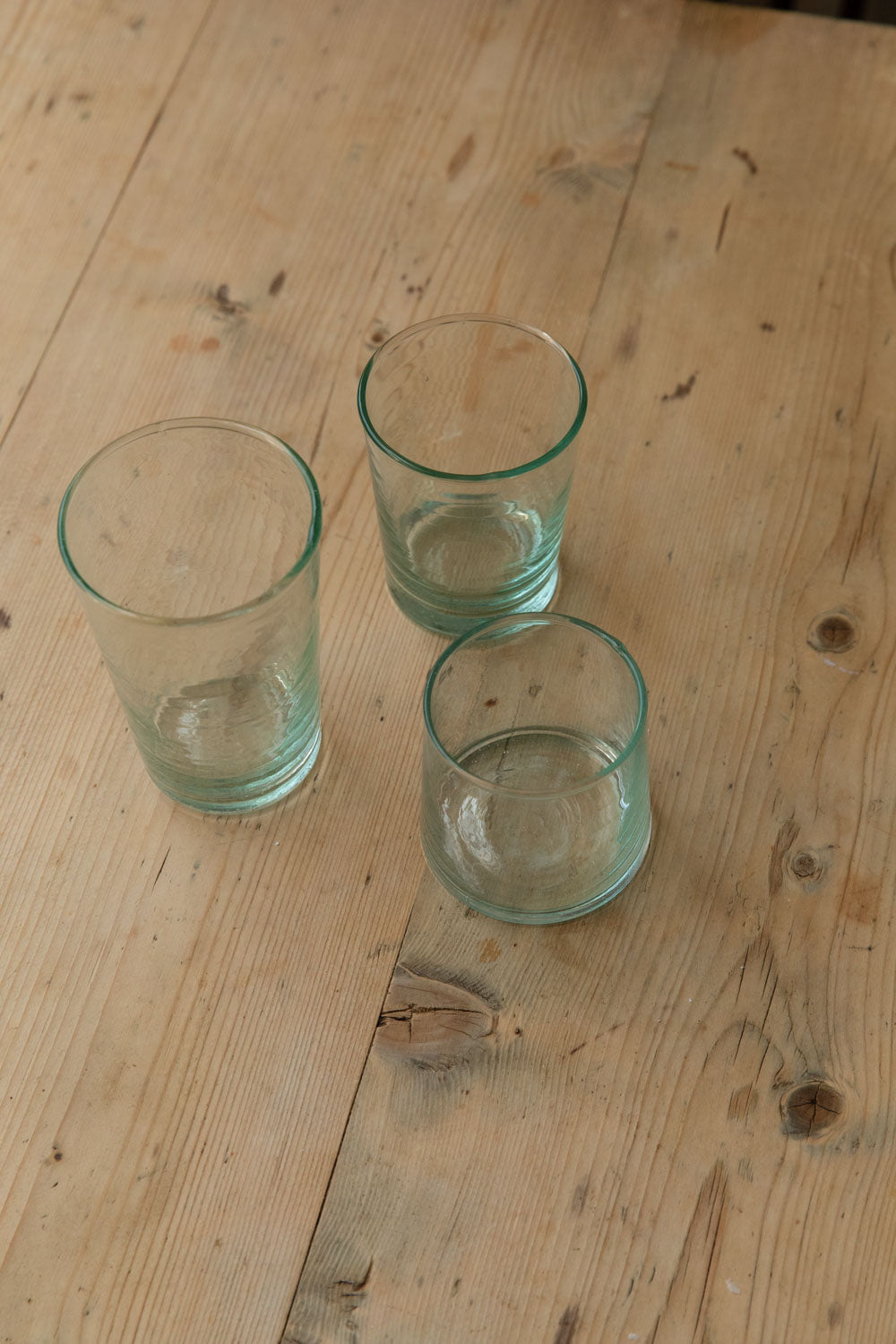 Three Meknes hand-blown recycled glass tumblers with gentle bubbles on a scrubbed table