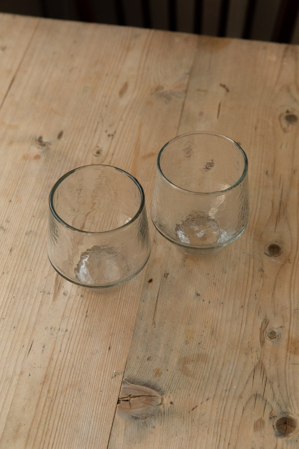 Two hammered tumbler glasses on a pale wooden table