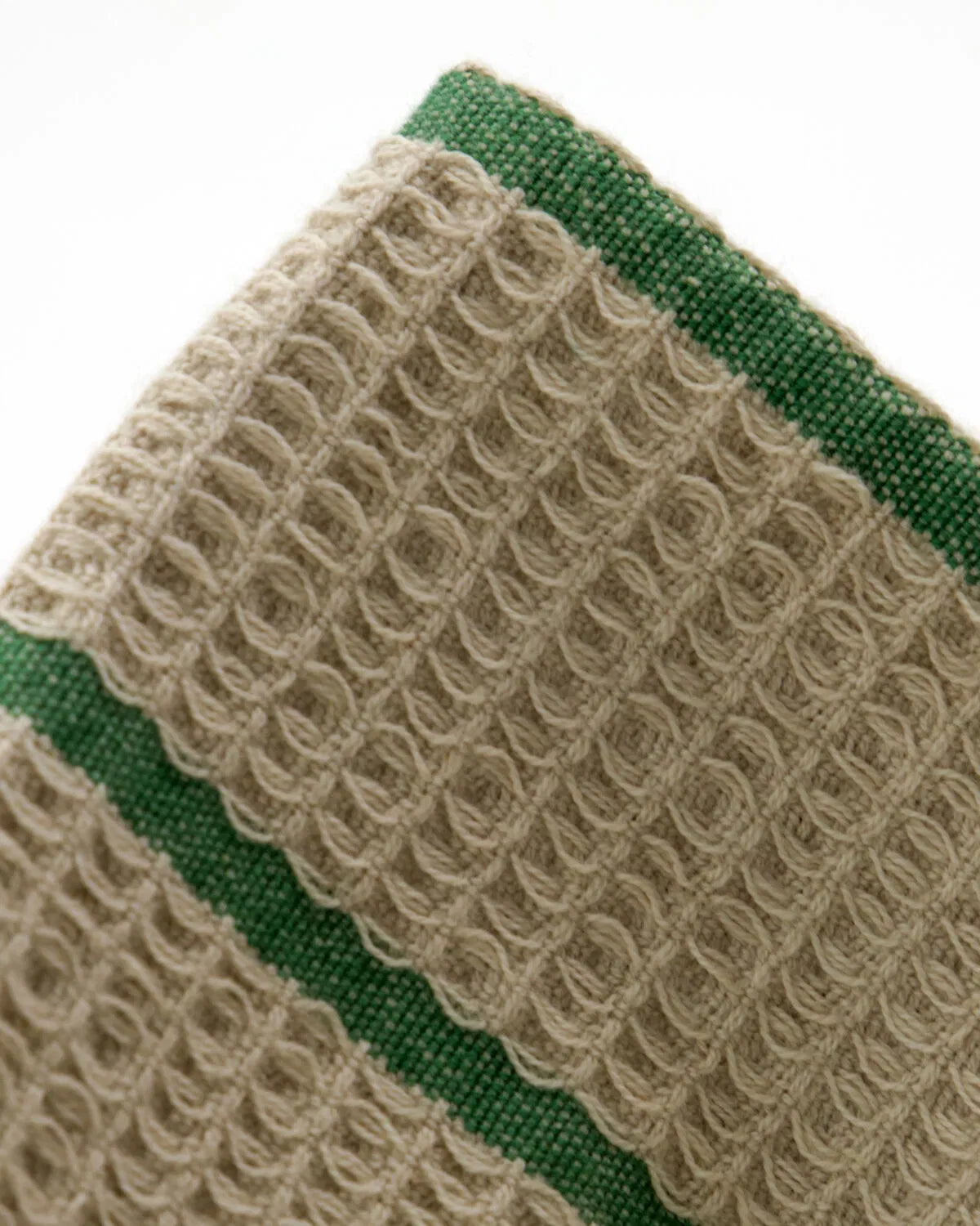 Close up showing the texture and colour of a sand and green striped Rena wash cloth, set against a white background.