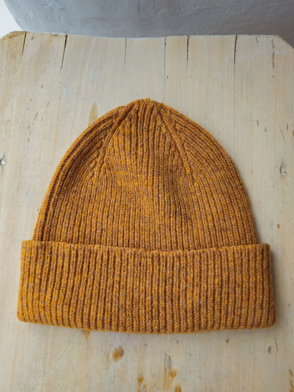 A mustard yellow ribbed knit beanie hat resting on a light-colored wooden surface.