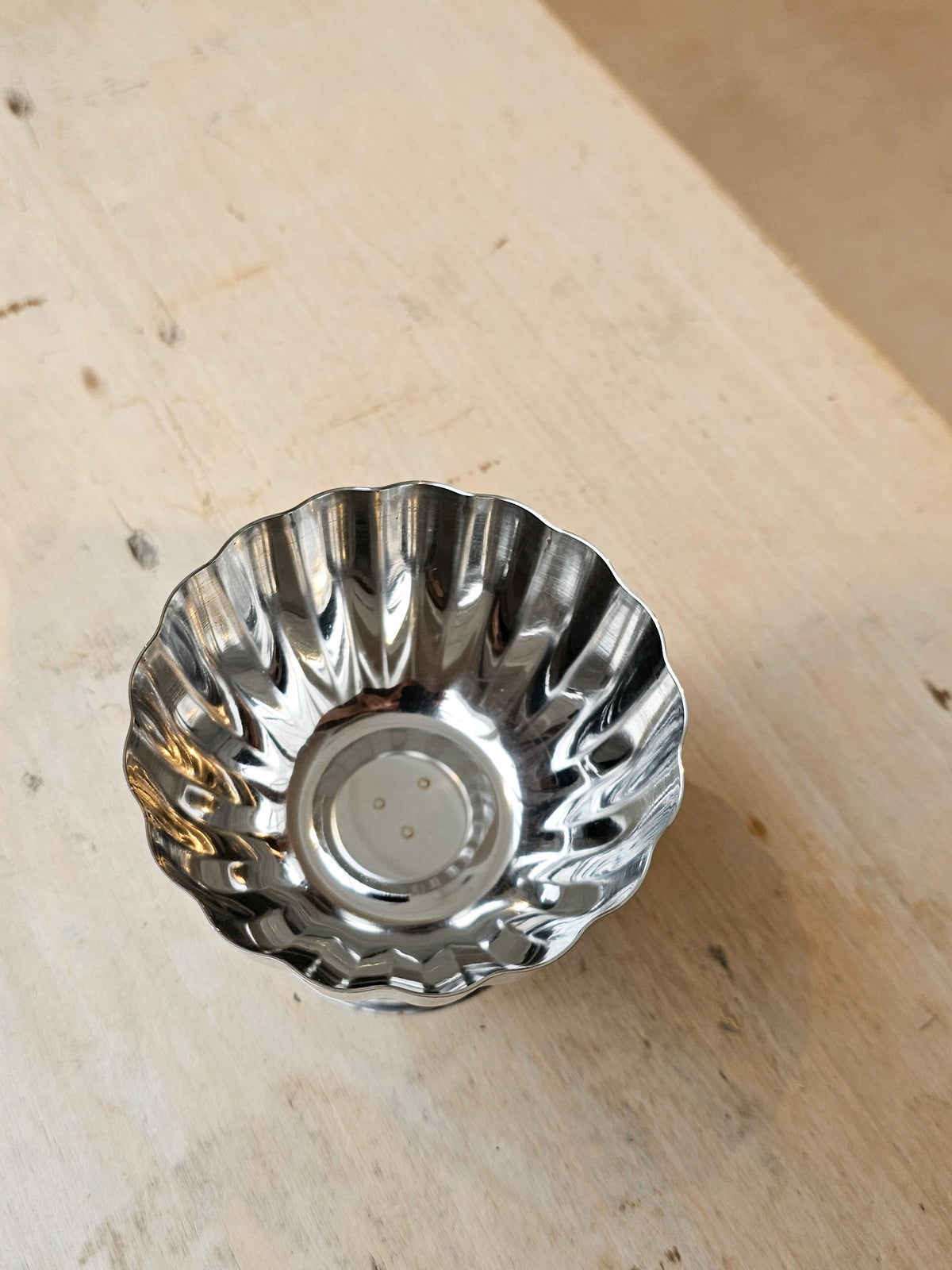 A small metallic silver bowl with a fluted, scalloped rim, photographed from above on a light wood surface.