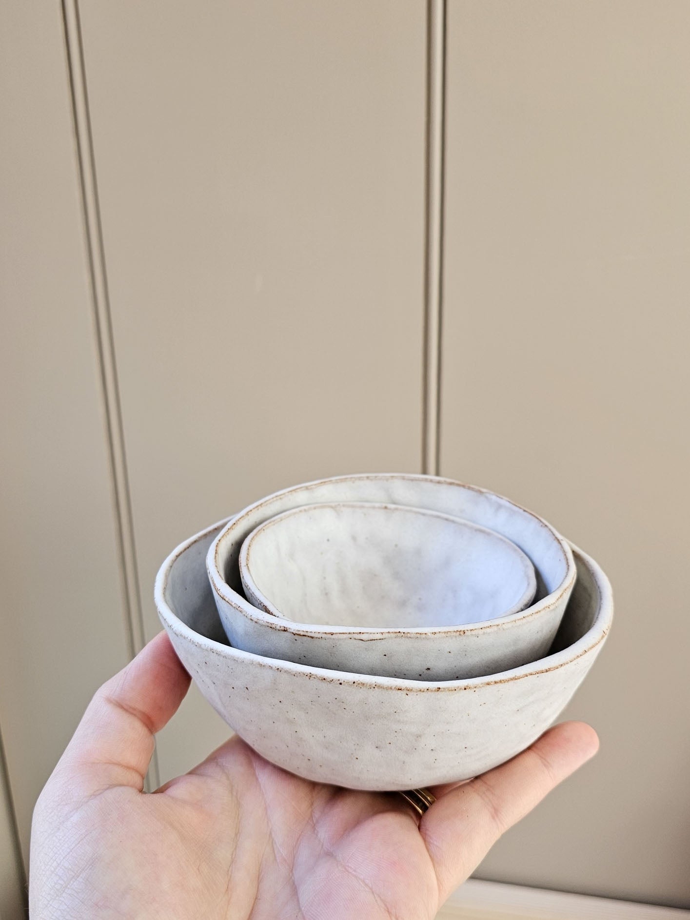 Hand holding three ceramic bowls against a neutral background