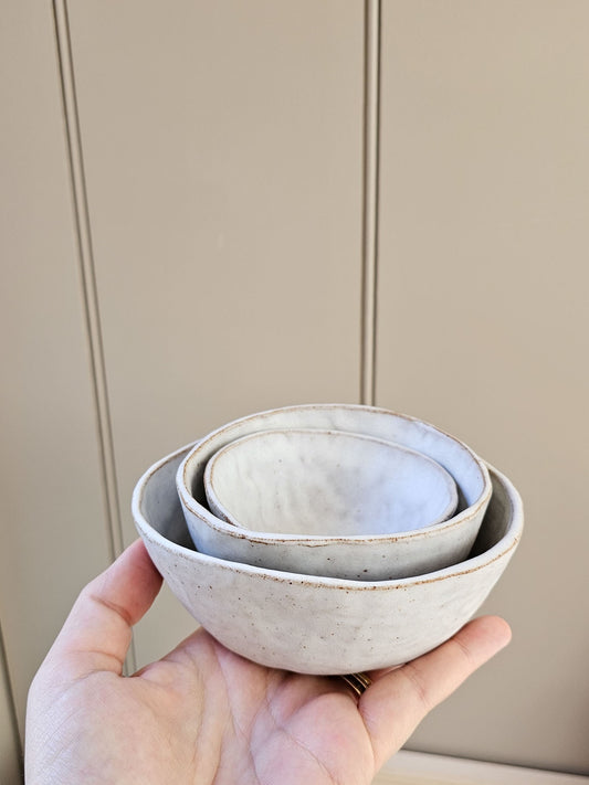 Hand holding three ceramic bowls against a neutral background