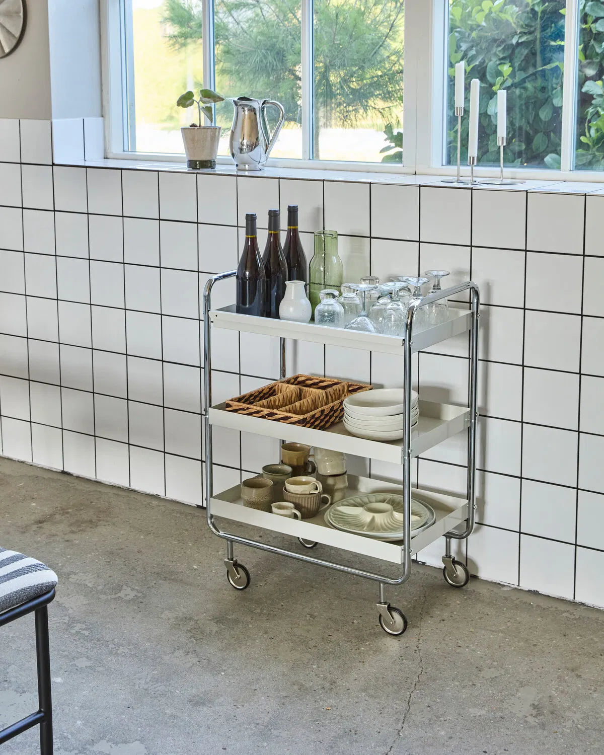 Large Roll storage trolley, shown in a kitchen setting, with a concrete floor and white subway tiles. The trolley is filled with various bottles, mugs, plates.