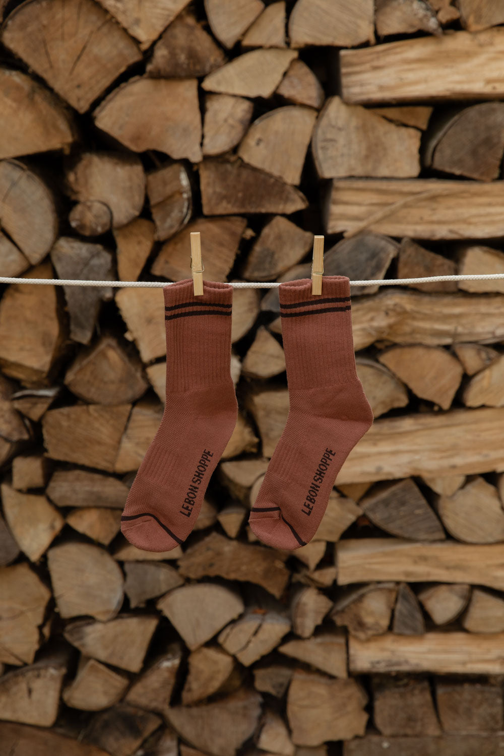 Le Bon Shoppe Boyfriend Socks in Clay with black stripes pegged on a line against logs