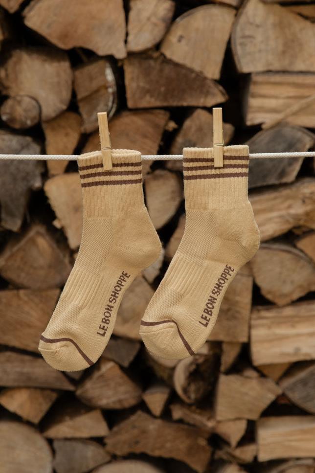 Le Bon Shoppe Girlfriend Socks in Daisy with brown stripes hanging from wooden pegs against stacked logs