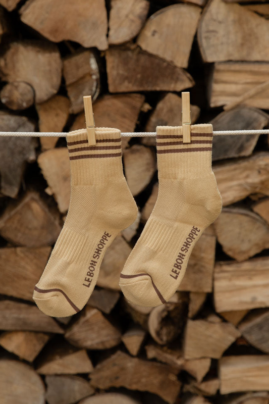 Le Bon Shoppe Girlfriend Socks in Daisy with brown stripes hanging from wooden pegs against stacked logs