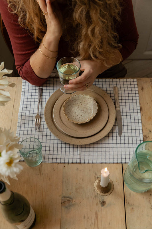 Woman with a glass of wine at a table set with speckled plates, a scalloped dish and a lit candle