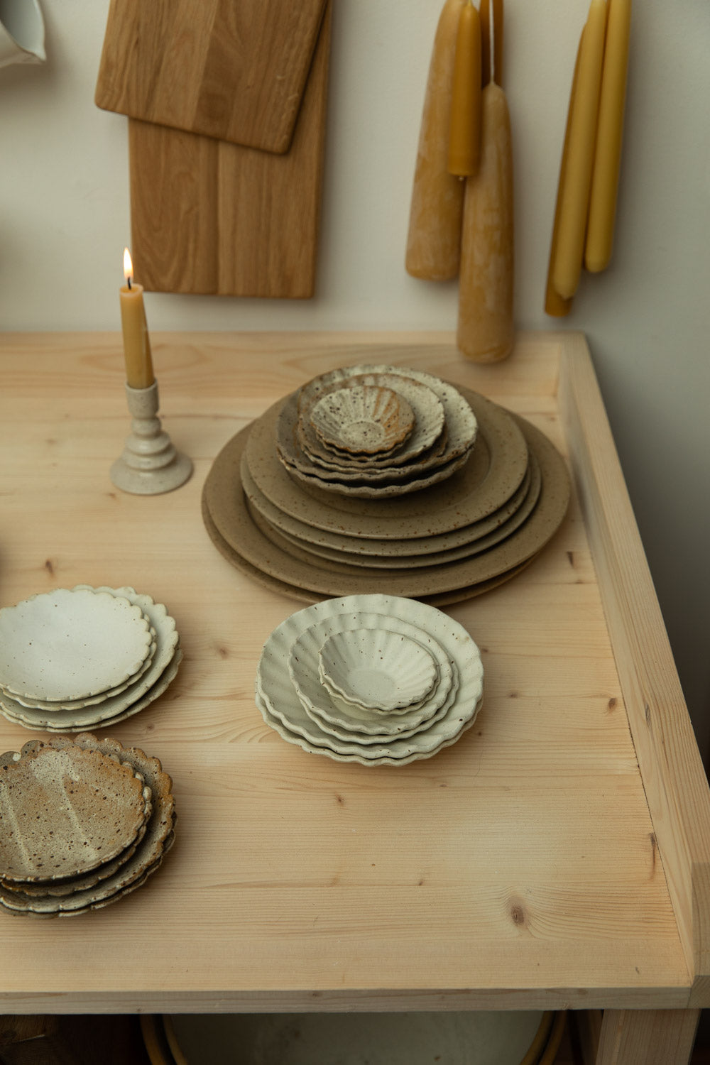 Set of ceramic plates on a wooden table with candles and wooden cutting boards in the background.