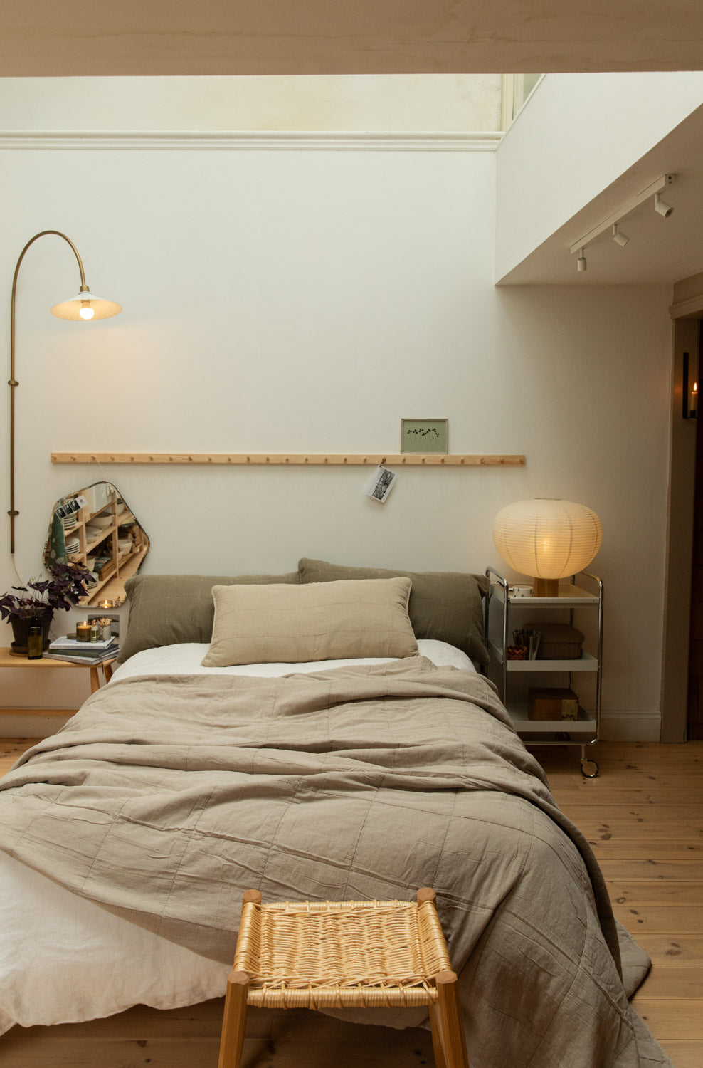Full Scandinavian bedroom with Blomus Kami lamp on chrome trolley, vintage linen cotton quilt, rattan oak stool at foot of bed and brass arc lamp.