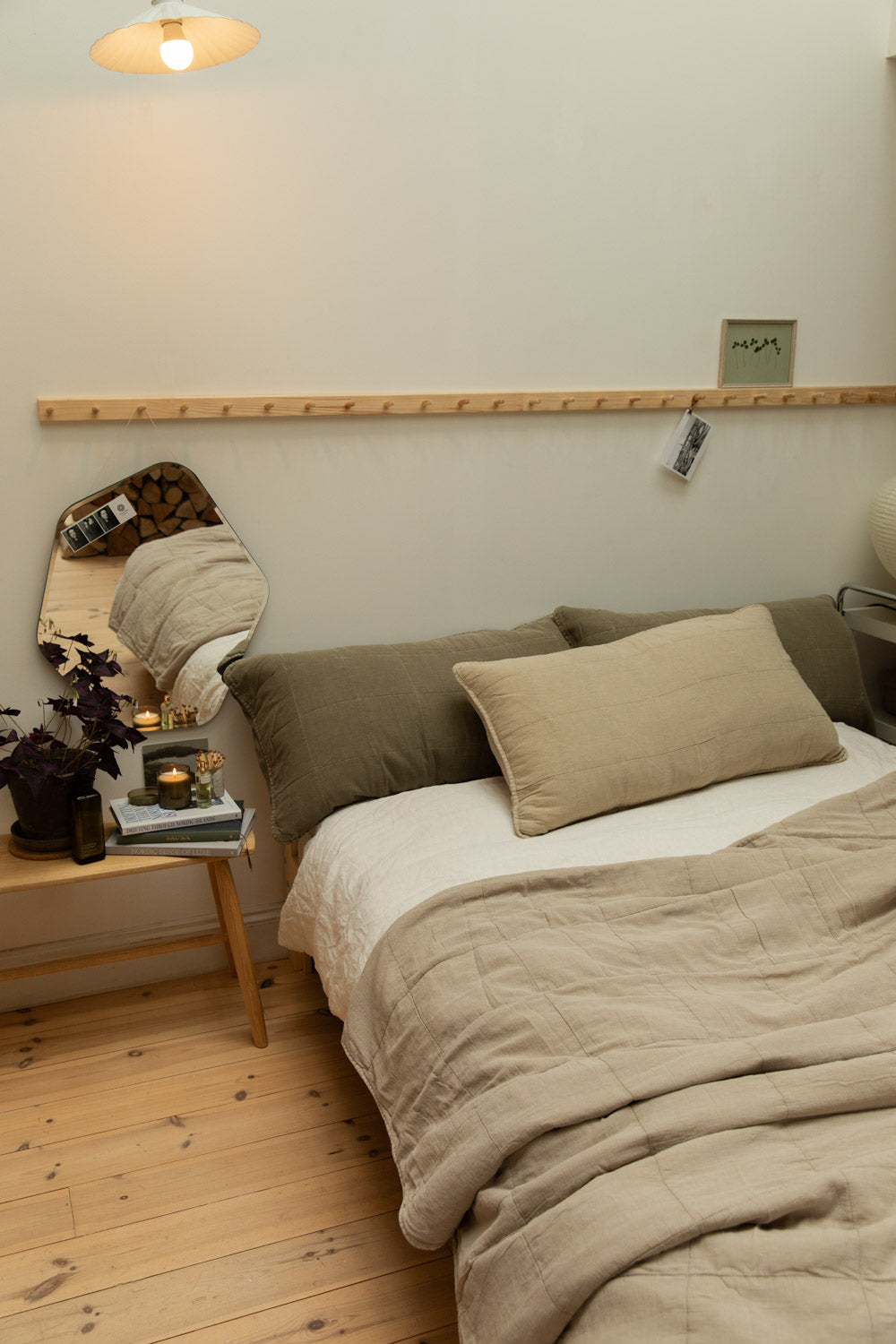 Warm Scandinavian bedroom with layered linen bedding, freeform mirror, peg rail wall, candles and oxalis plant on pine floor