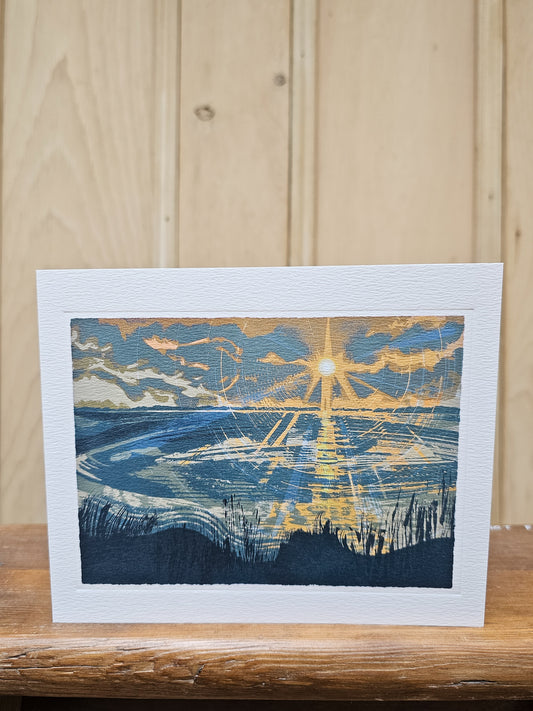 Greeting card reproducing a linocut print of a sunset over the Severn Estuary, with dramatic rays of golden light reflected across the water and dark grasses in the foreground