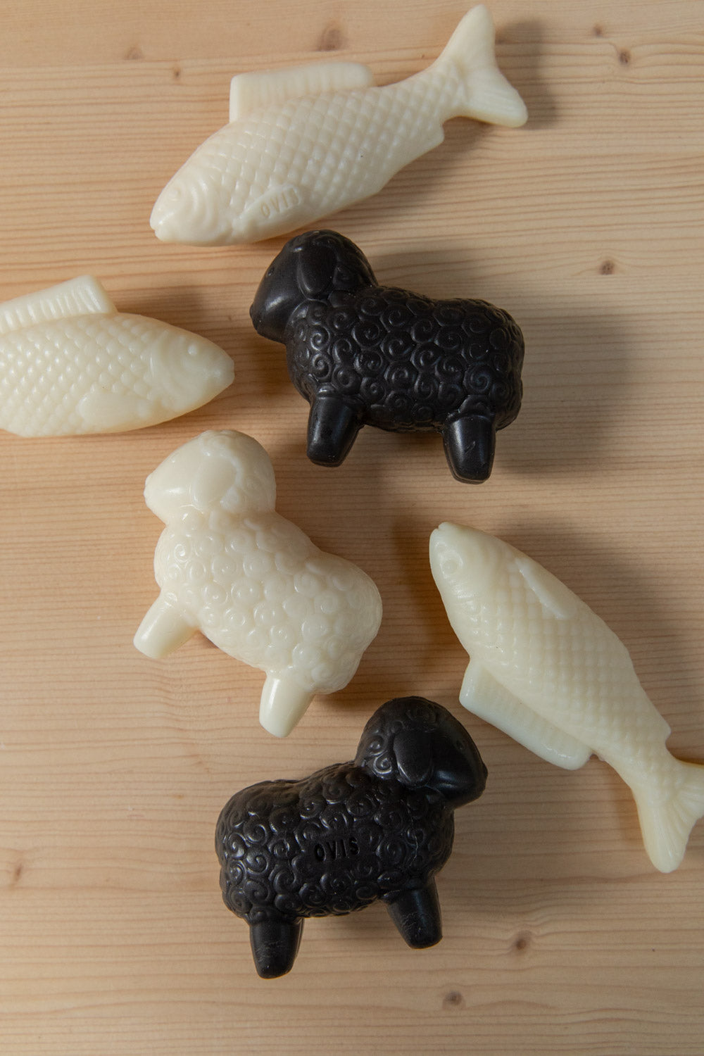 White and black sheep-shaped soaps and white fish soaps scattered on pine