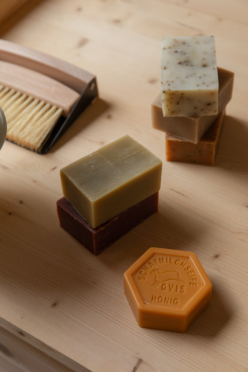 Hexagonal sheep's milk honey soap in front of stacked soap bricks and a wooden brush